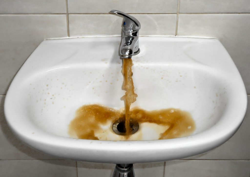 Trübes Wasser läuft aus einem Wasserhahn — sichtbare Sediment- und Rostpartikel im Trinkwasser