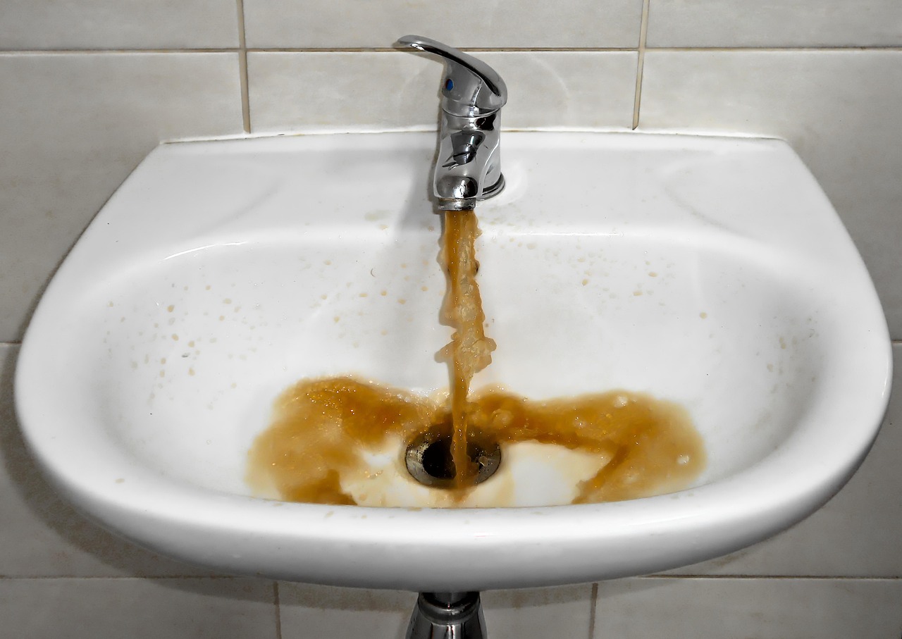Trübes Wasser läuft aus einem Wasserhahn — sichtbare Sediment- und Rostpartikel im Trinkwasser